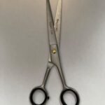 7-inch-professional-barber-scissors-stainless-steel-razor-edge.jpg  "Close-up of professional 7-inch barber scissors with silver stainless steel blades and an ergonomic offset handle."  barber-using-7-inch-shears-for-scissor-over-comb.jpg "Professional barber performing a scissor-over-comb technique using 7-inch hair cutting shears."  razor-edge-hollow-ground-blade-detail.jpg "Macro shot of the hand-honed razor edge on high-carbon steel barber scissors."